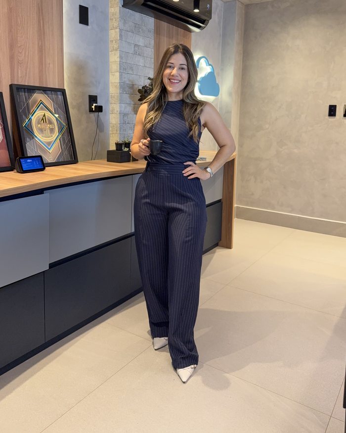 Thaís Hipólito standing in her studio, smiling and holding a cup of coffee